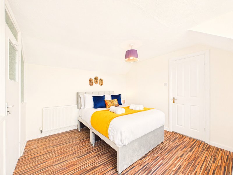 Bright bedroom with white bed, yellow and blue bedding, wooden floor and pendant light