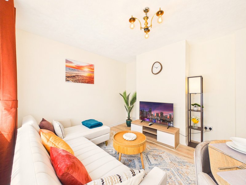Bright living room with white sofa, wooden coffee table, TV unit, and colorful cushions