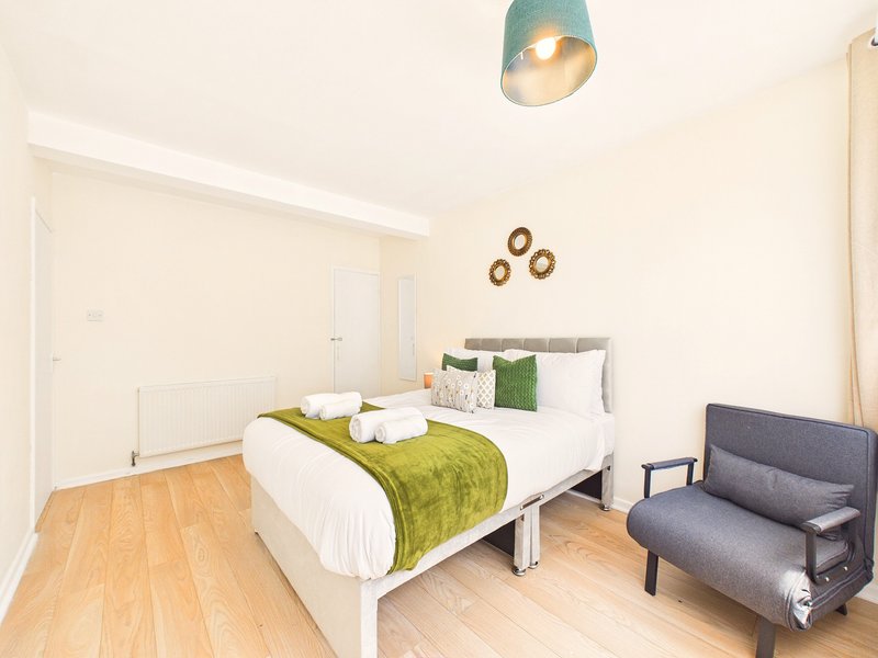 Bright bedroom with double bed, green throw, white pillows, wooden floor and armchair