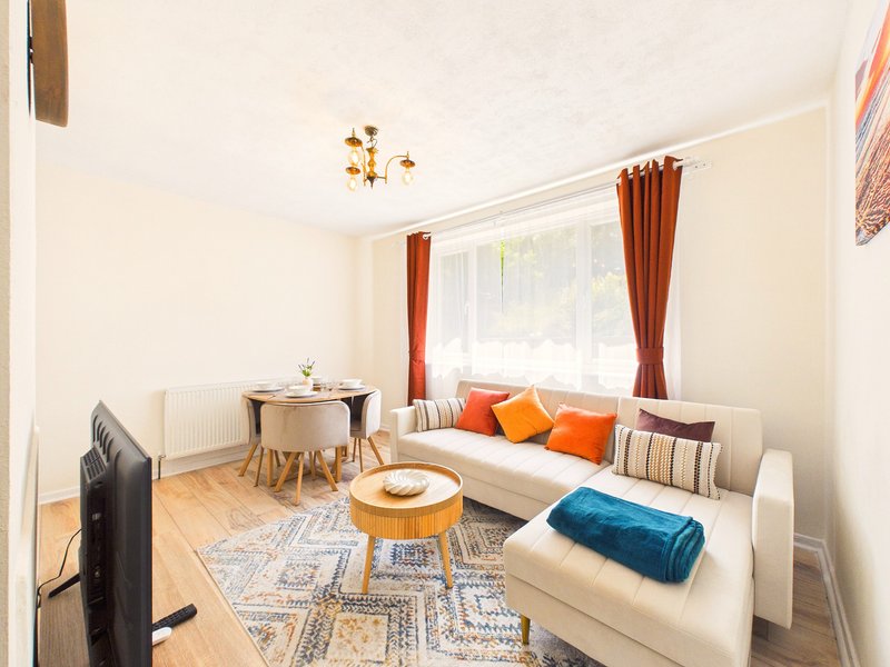 Bright living room with cream sofa, orange and blue cushions, wooden coffee table and window with red curtains