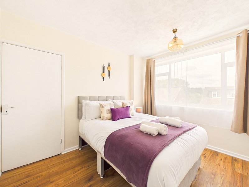 Bright bedroom with double bed, purple throw, white pillows and wooden flooring