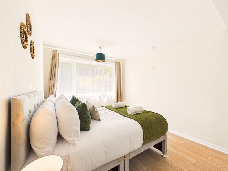 Bright bedroom with double bed, white bedding, green cushions and decorative wall plates