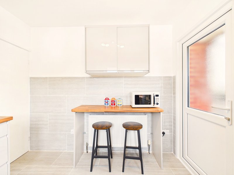 Modern kitchen with white cabinetry, subway tile backsplash, wooden countertop and bar seating