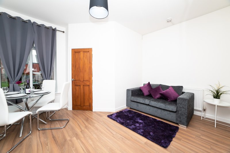 Modern living room with gray sofa, purple cushions, wooden floor and dining area