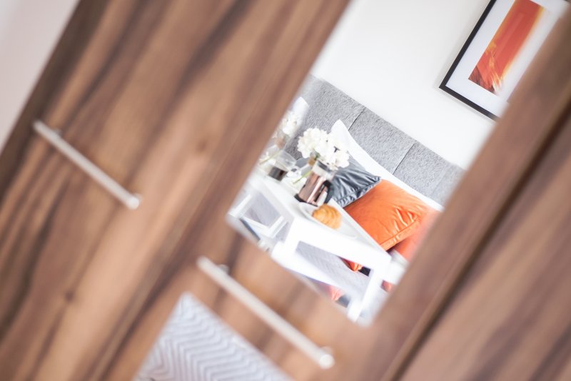 Bedroom interior viewed through open doorway, showing bed with orange and gray bedding and wall art