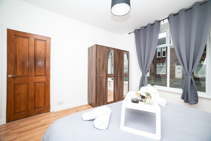 Bright bedroom with double bed, wooden wardrobe, wooden doors and grey curtains