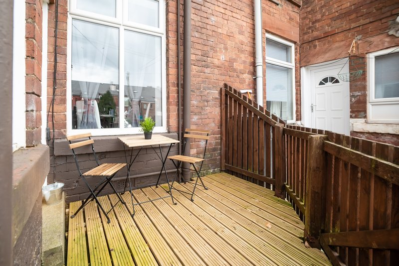 Wooden decked balcony with table, chairs, potted plant and brick building exterior
