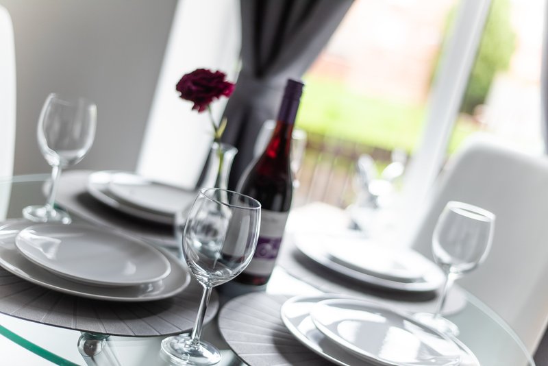 Formal dining table set with wine glasses, plates, and dark red flower arrangement