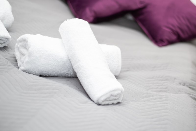 Rolled white towels on bed with purple pillows in background