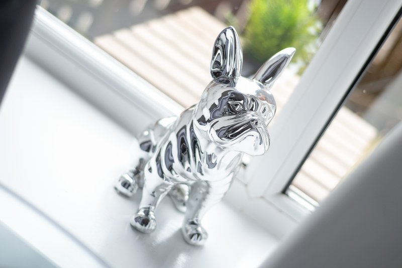 Silver decorative dog figurine on white windowsill with natural light