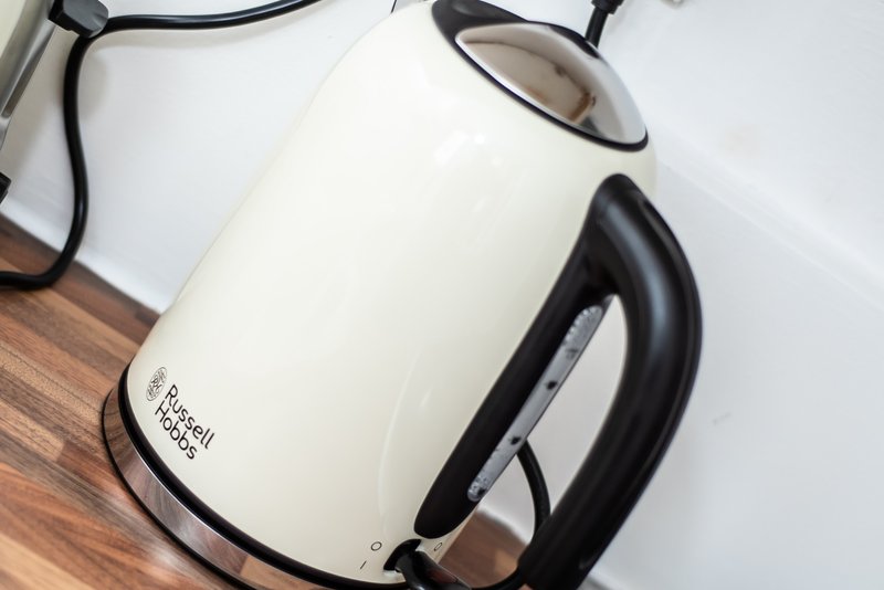 White and black electric kettle on wooden surface with cord