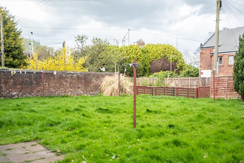 Open garden with grass, brick wall, wooden fencing and brick building