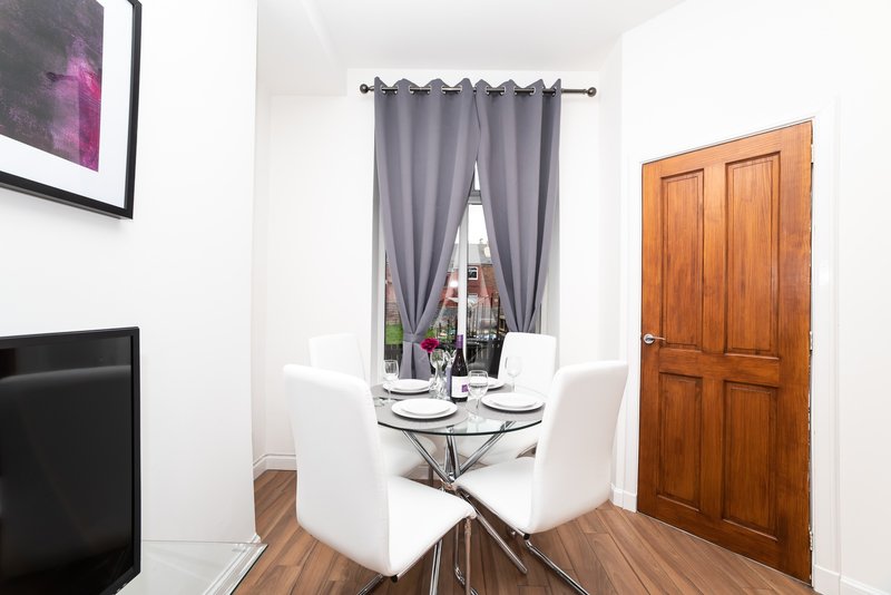 Dining area with round glass table, white chairs, gray curtains and wooden door