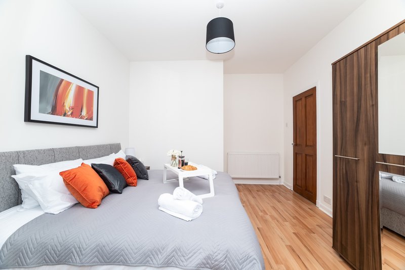 Modern bedroom with gray bed, orange cushions, wooden flooring and wall art
