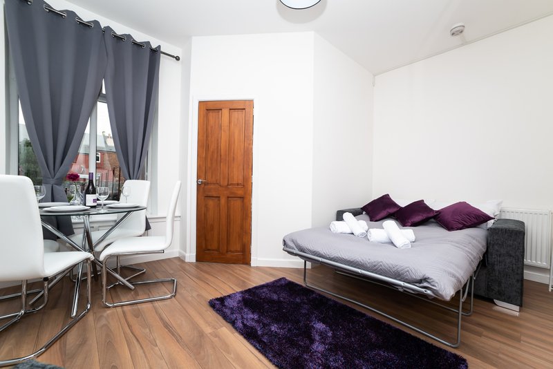 Studio bedroom with bed, desk, chair, wooden flooring and purple accents