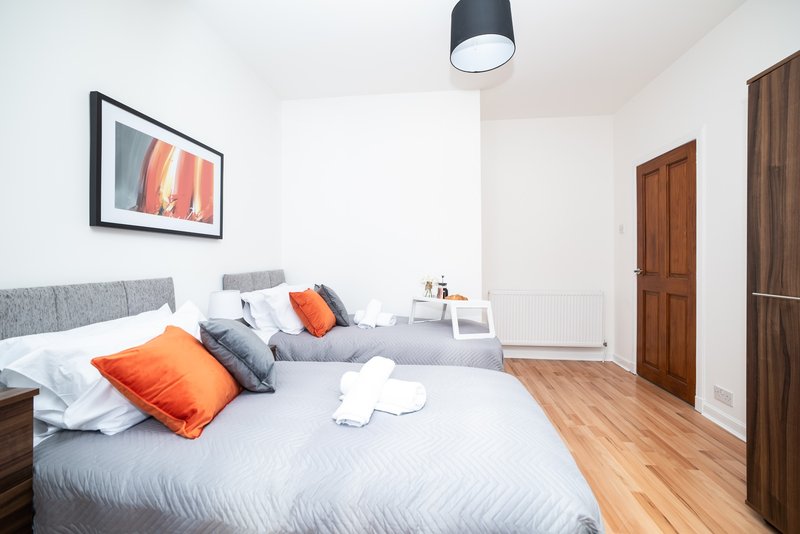 Modern bedroom with grey double bed, orange pillows, wooden floor and pendant light