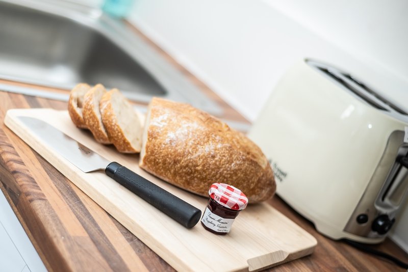 Kitchen counter with sliced bread, knife, jam jar and milk carton