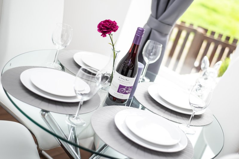 Formal dining table set for two with wine bottle, glasses, plates and pink flower centerpiece