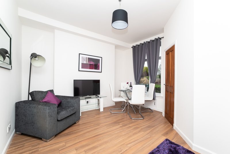 Modern living room with grey armchair, TV unit, desk, wooden flooring and pendant light