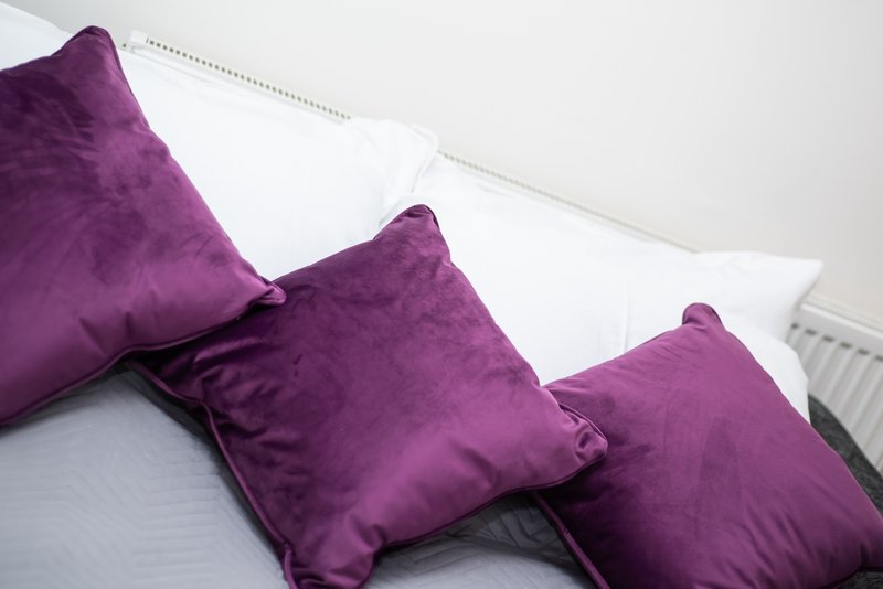 Bed with purple velvet cushions and white pillows against white headboard