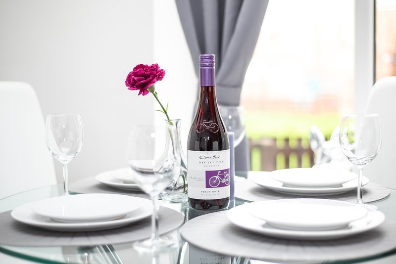 Formal dining table set with wine bottle, glasses, pink flower and place settings