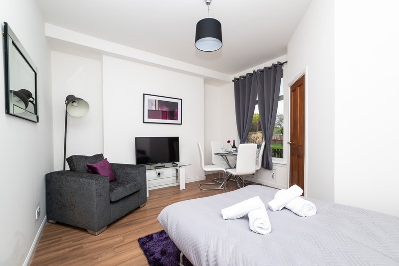 Studio bedroom with double bed, grey armchair, desk, TV and pendant light