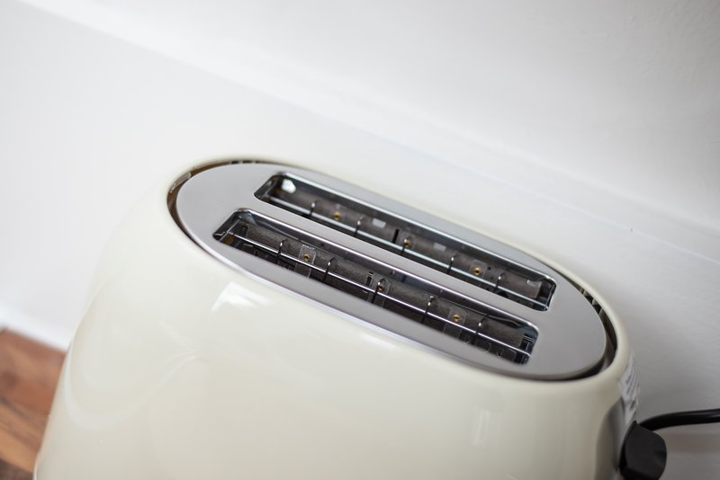 Close-up of white toaster with heating slots and black cord on white surface