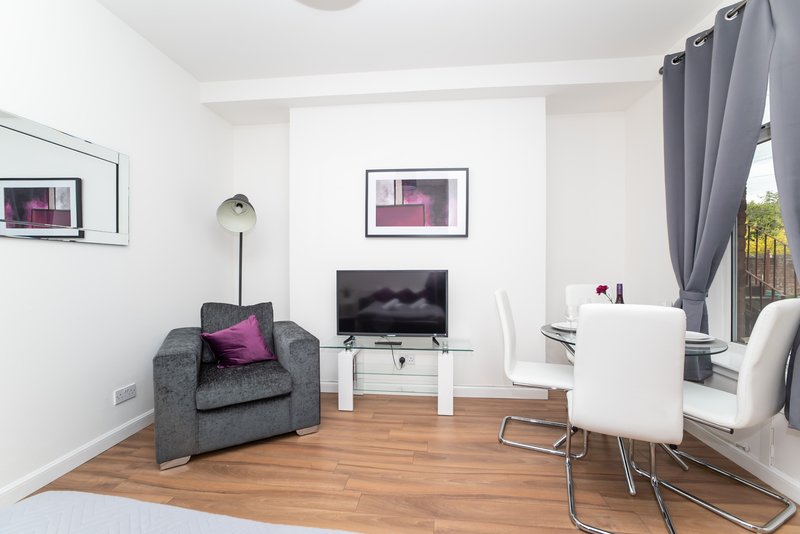 Modern living room with gray armchair, TV on stand, white chair, and wooden flooring