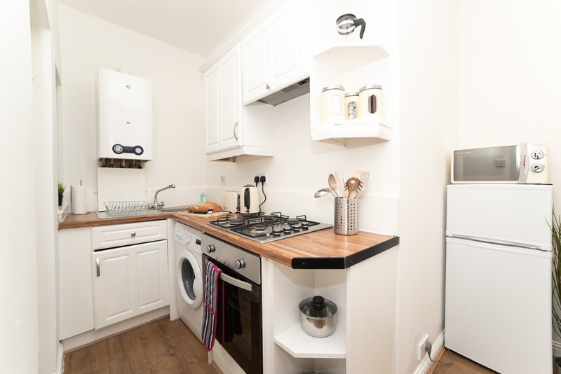 Small compact kitchen with white cabinetry, wooden worktop, gas hob, and integrated appliances