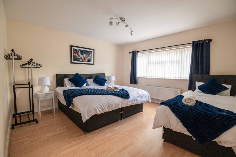 Spacious bedroom with two beds, dark blue bedding, wooden floor and large window