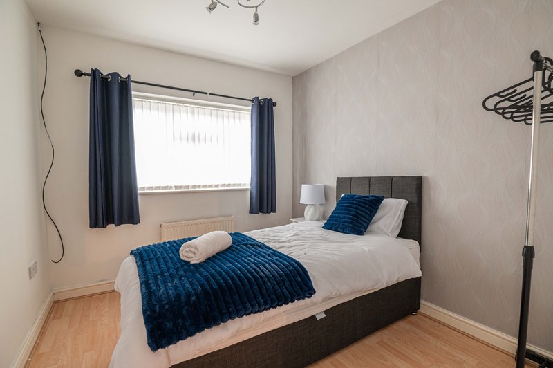 Bedroom with double bed, blue bedspread, dark headboard, window with navy curtains