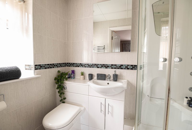 Modern bathroom with white vanity, round mirror, toilet, and walk-in shower enclosure