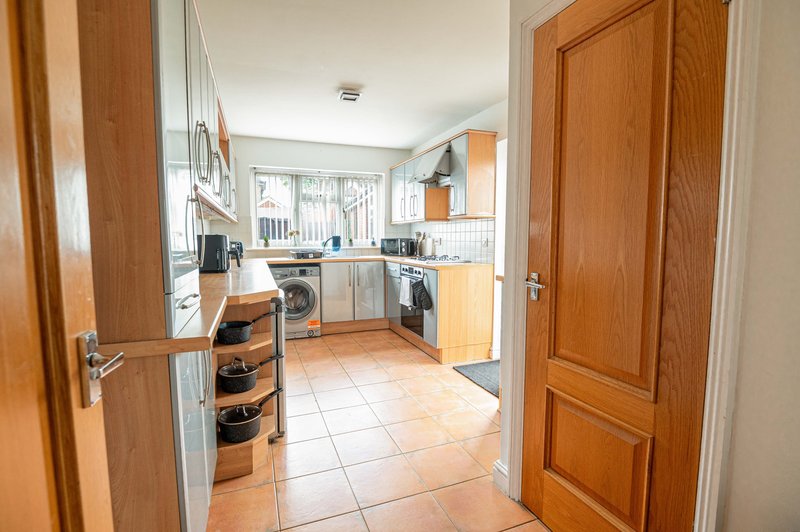Kitchen with wooden cabinetry, tiled floor, washing machine and countertops with appliances