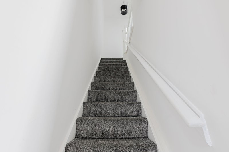 Staircase with gray carpet, white walls, handrail and ceiling light fixture