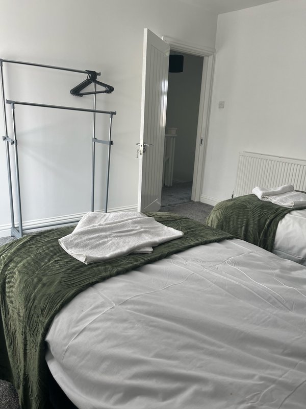 Bedroom with two beds, green quilts, white pillows, clothing rack and open door