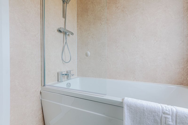 Modern bathroom with white bathtub, glass shower enclosure and beige tiled walls