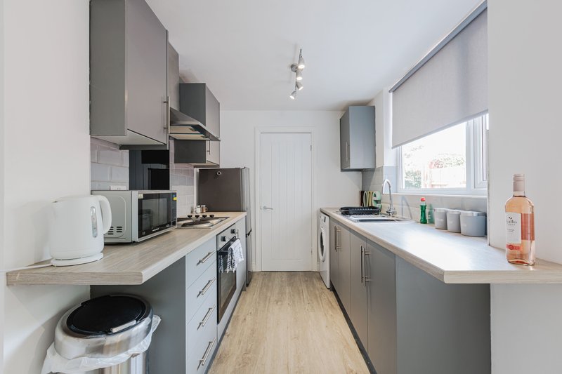 Modern galley kitchen with grey cabinetry, white countertops, and stainless steel appliances