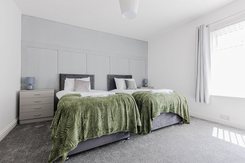 Modern bedroom with two single beds, green bedspreads, wooden nightstands and panelled headboard
