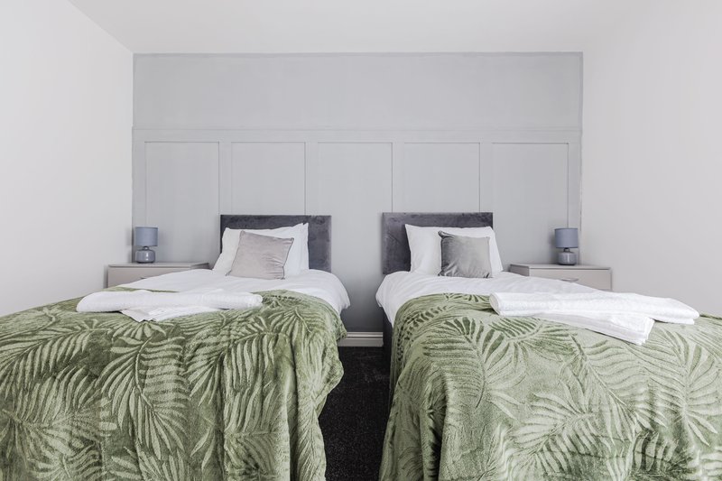 Twin bedroom with two single beds, green patterned throws, grey headboard and bedside lamps