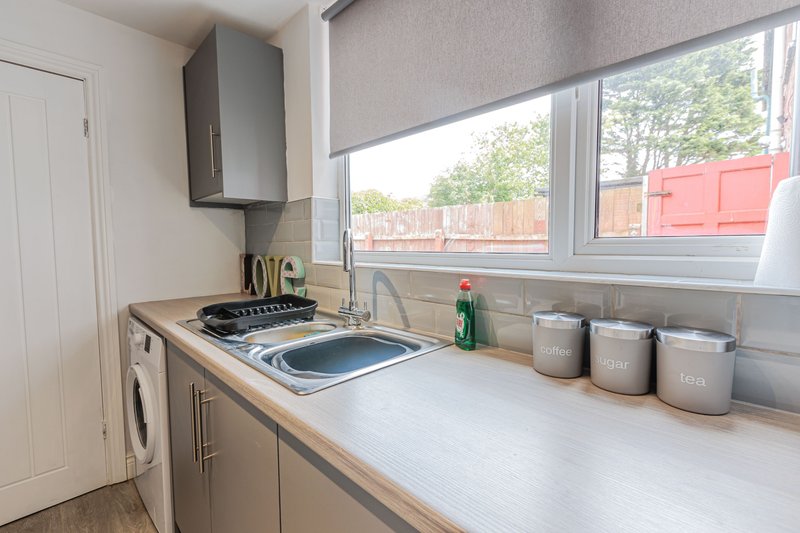 Modern kitchen with cooktop, extractor hood, windowsill storage jars and garden view