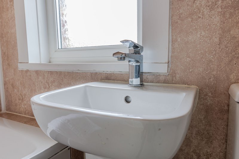 Modern bathroom with white curved sink, chrome faucet, and mirror above window