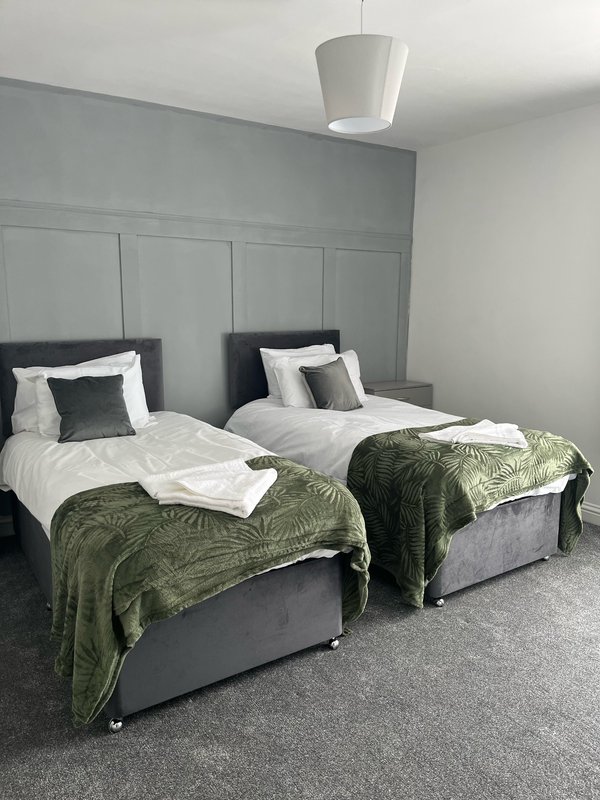 Twin bedroom with grey headboards, white bedding, green throws, and pendant light