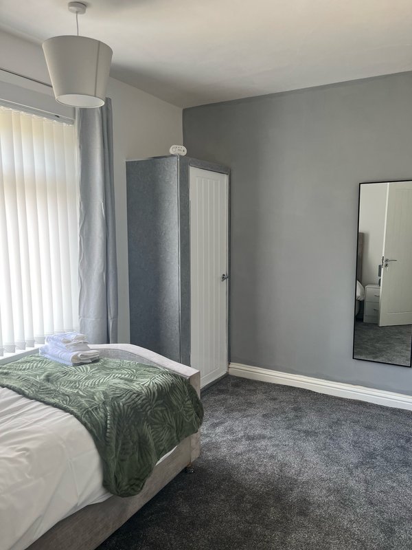 Modern bedroom with double bed, green throw, pendant light, and gray carpet flooring