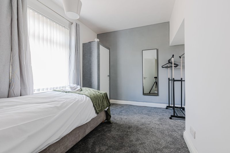 Modern bedroom with double bed, grey carpet, pale walls, and clothes rail by window