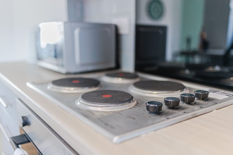 Modern kitchen cooktop with four burners and control knobs, microwave and appliances visible