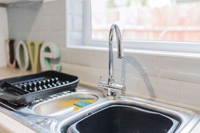 Kitchen sink with chrome faucet, grater, and decorative letters by window