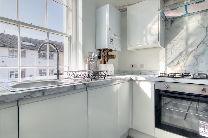 Modern white kitchen with marble countertop, gas stove, sink and window overlooking street