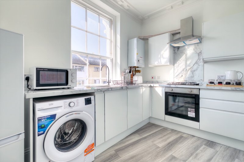 Modern white kitchen with washing machine, oven, hob, and large window overlooking street