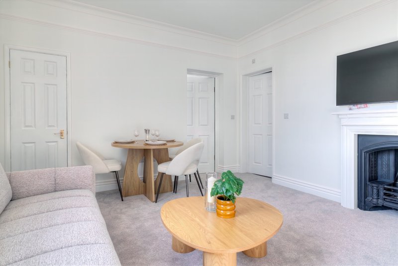 Bright living room with sofa, wooden dining table, chairs, fireplace and wall-mounted TV