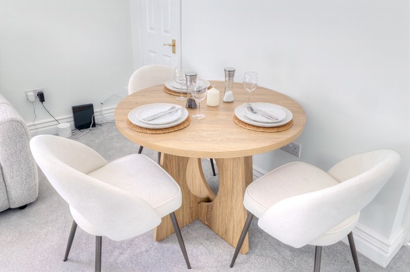 Dining area with round wooden table, white upholstered chairs, place settings, and glassware